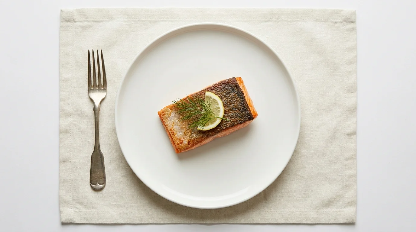 A beautifully plated salmon dish on a white plate with elegant silver cutlery, emphasizing artistic food presentation.