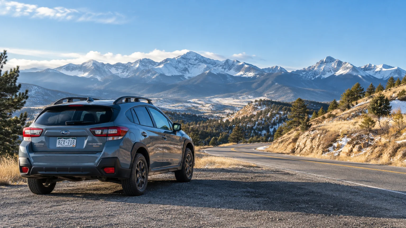 A blue SUV parked on the shoulder of a paved mountain road overlooking snow-capped peaks under a blue sky.