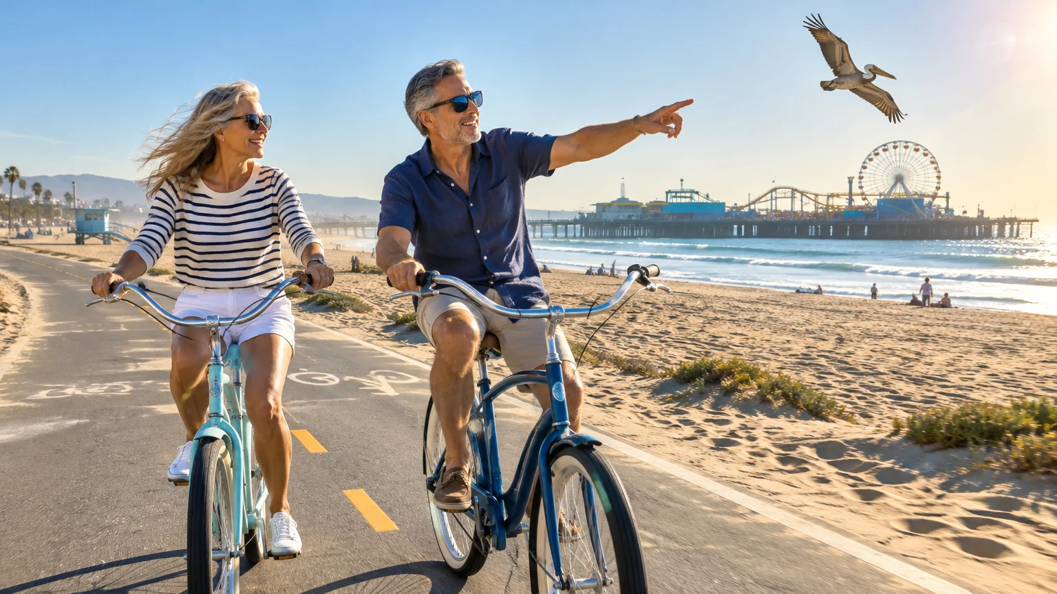 Mature couple riding cruiser bicycles along a beachside paved path with the Santa Monica Pier in the background.